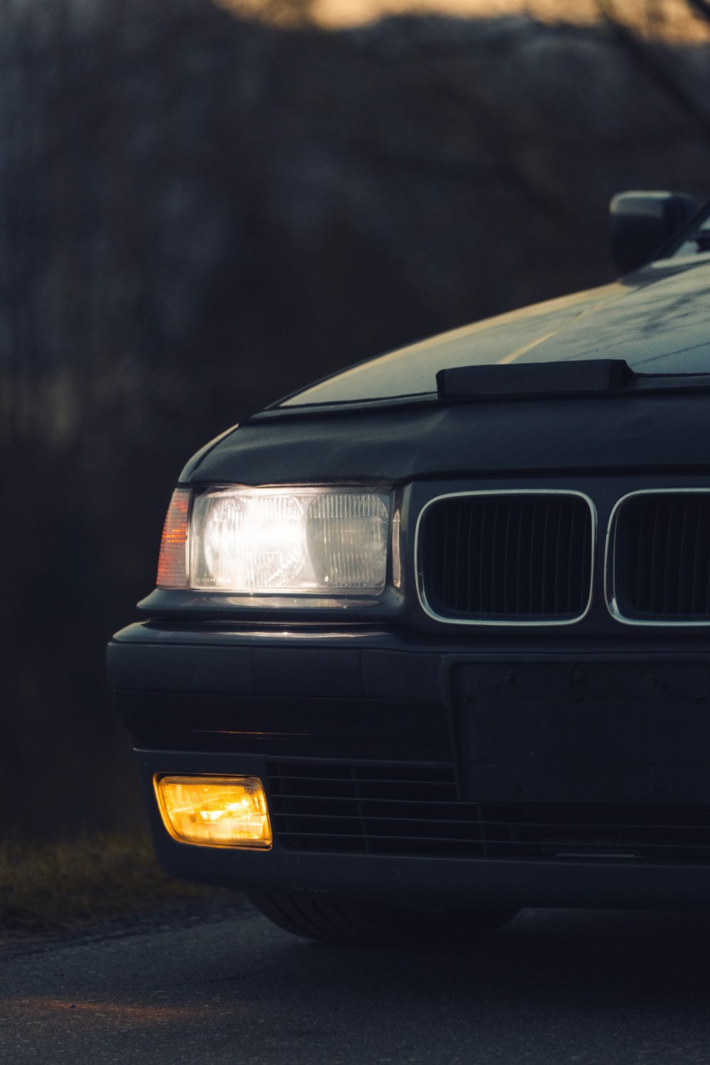 Illuminated headlight and lower fog light on a BMW E36 at dusk